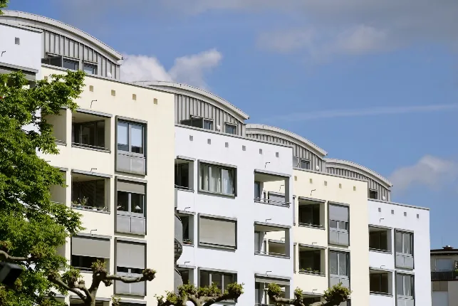 Mehrstöckiges Wohngebäude mit hellen Fassaden, Balkonen und modernen Runddächern unter blauem Himmel